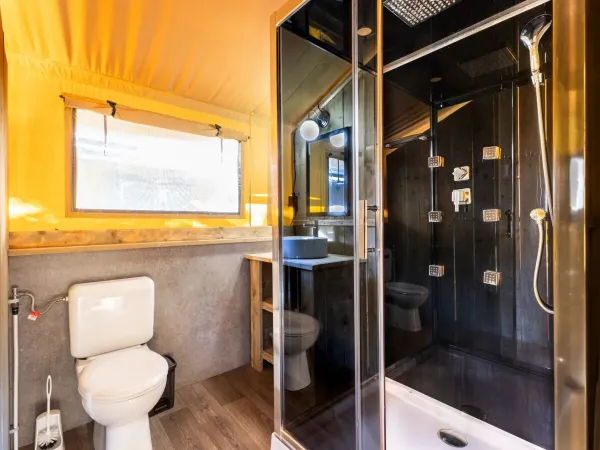 Il bagno del Roan Lodgetent Premium XL è dotato di cabina doccia di lusso, WC e lavabo.