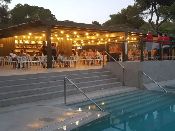 Terrazza a bordo piscina la sera al campeggio Roan Cala Gogo.