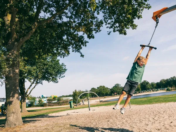 Bambino che si dondola sulla corda nel parco giochi del campeggio Roan di Schatberg.