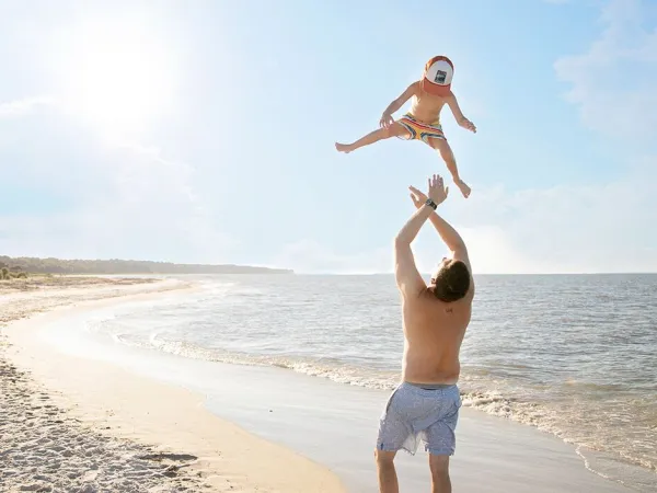 Il padre lancia il figlio in aria sulla spiaggia del campeggio Roan Sole Family Camping Village.