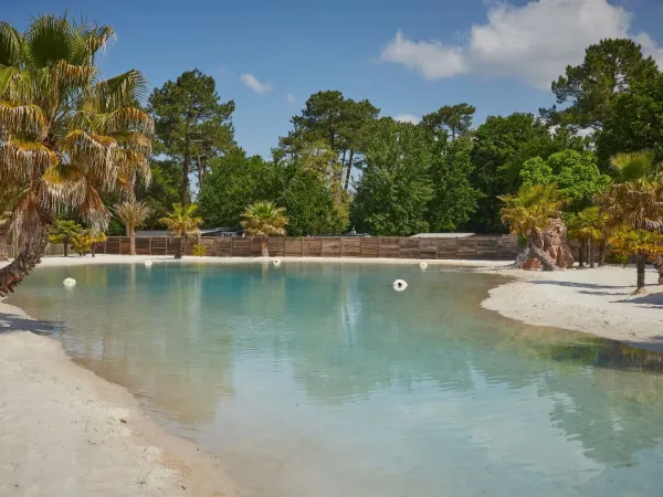 La piscina laguna tropicale con palme e spiaggia sabbiosa del campeggio Roan La Clairière