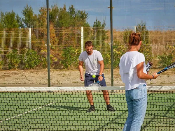2 persone giocano una partita di tennis al Roan camping Les Dunes.