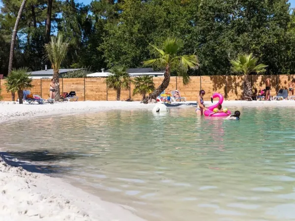 Persone che prendono il sole presso la piscina della laguna del campeggio Roan La Clairière.