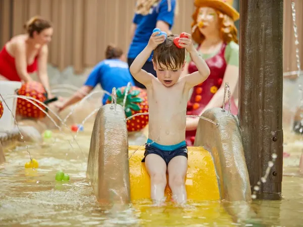 Bambino che si diverte in acqua dallo scivolo della piscina per bambini del campeggio Roan Terspegelt.