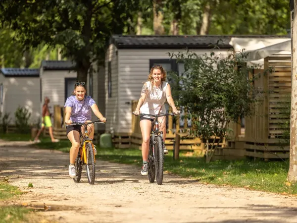 2 signore attraversano in bicicletta il campeggio Roan Château de Galaure.