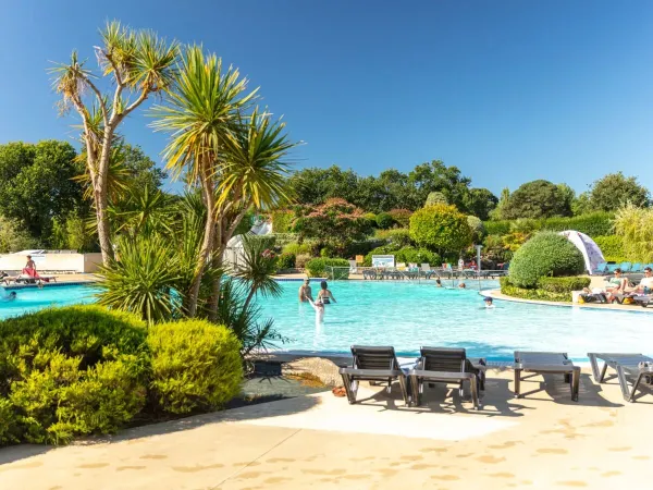 La piscina con lettini e il bellissimo giardino del campeggio Roan La Grande Métairie.