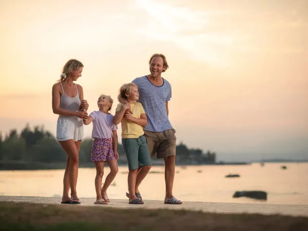 Famiglia sorridente che passeggia sulla spiaggia al tramonto.