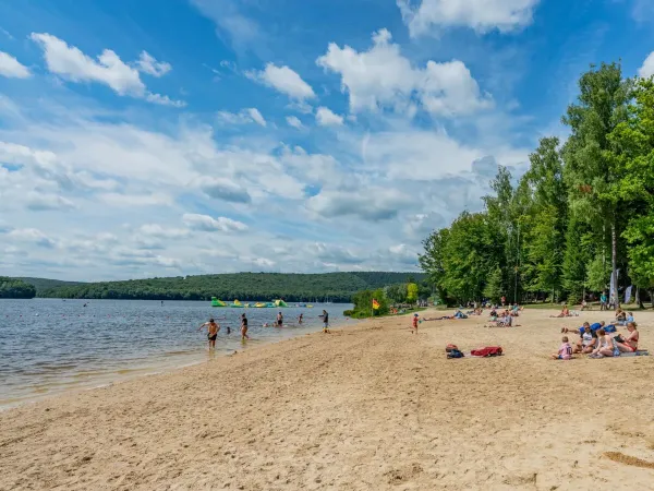 Le famiglie prendono il sole sulla spiaggia del lago al campeggio Roan Le Lac des Vieilles Forges.