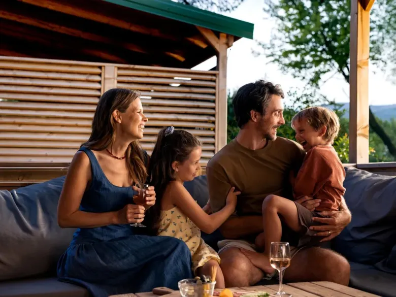 Padre e figli si divertono sul divano della casa mobile del campeggio Roan Le Petit Mousse.